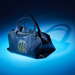 Green leather sports bag with yellow emblem. Blue lit background.