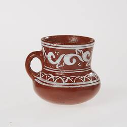 Miniature brown ceramic urn with handle. Features painted white patterns.