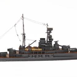 Wooden grey naval ship model with central tower, mast, mounted guns on wooden decks. Profile.