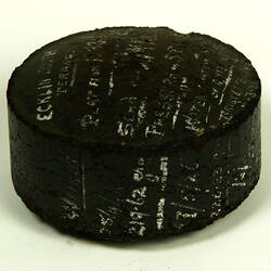 Black cylinder with white handwritten inscription.