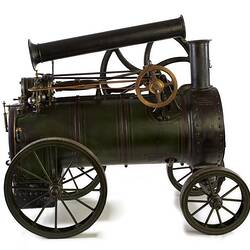 Model of black moveable steam engine on four wheels with tall folded back chimney at front.