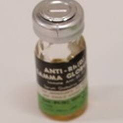 Glass vial with black, green and white label. Silver top.