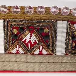 Detail of red fabric crown decorated with clear beads and trimming.
