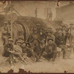 Group of construction workers pose on rocky worksite with machinery behind them.