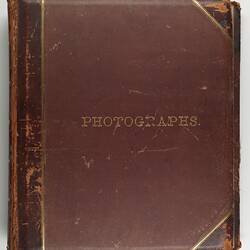 Worn brown photograph album with gold letters.