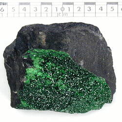 Grey rock with green crystals covering one face.