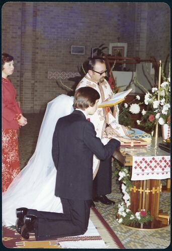 Profile of bride and groom kneeling in front of altar for their matrimonial ceremony. Father stands beside them.