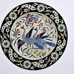 White plate, black edge featuring an elaborate design of two blue peacocks and flowers.