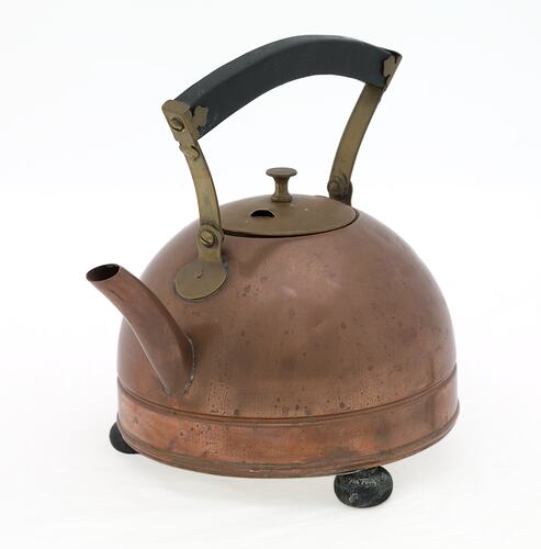 Domed copper kettle with brass lid, handle and badge. Black bakelite handle grip. Three black wooden feet.