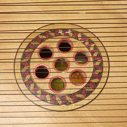 Detail of timber multi-stringed instrument. Pale wood. Central sound hole with 7 internal holes.