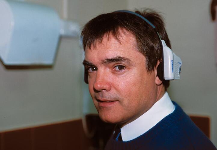 Close-up of Michael Greenwood wearing remote transceiver headset, in kitchen. Melbourne Coastal Radio Station, Cape Schanck, Victoria
