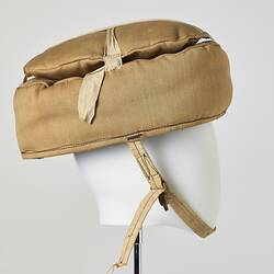 Beige cotton cap, padded, with strap. Profile.