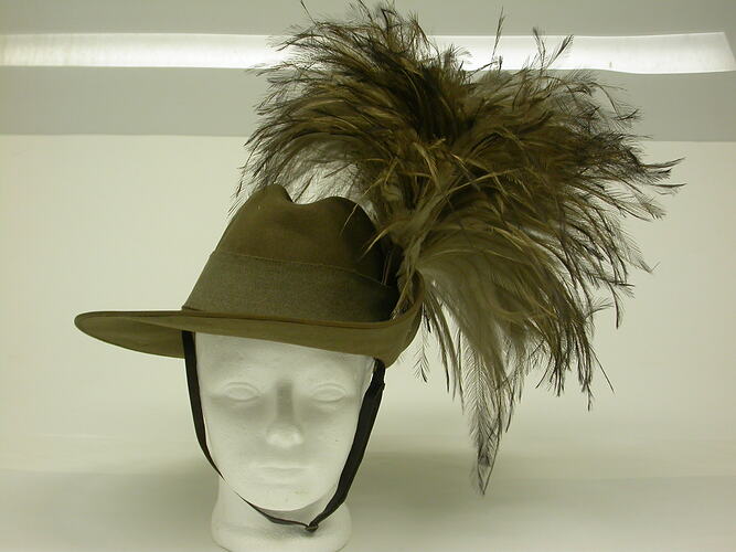 Green khaki hat with feather plum, on white mannequin head, front view.