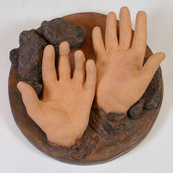 Circular sculpture of two clay hands.
