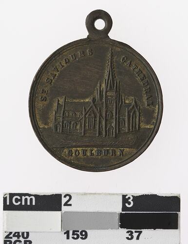 Round bronz coloured medal with building and text.