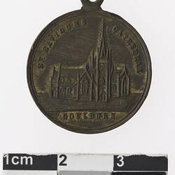 Round bronz coloured medal with building and text.
