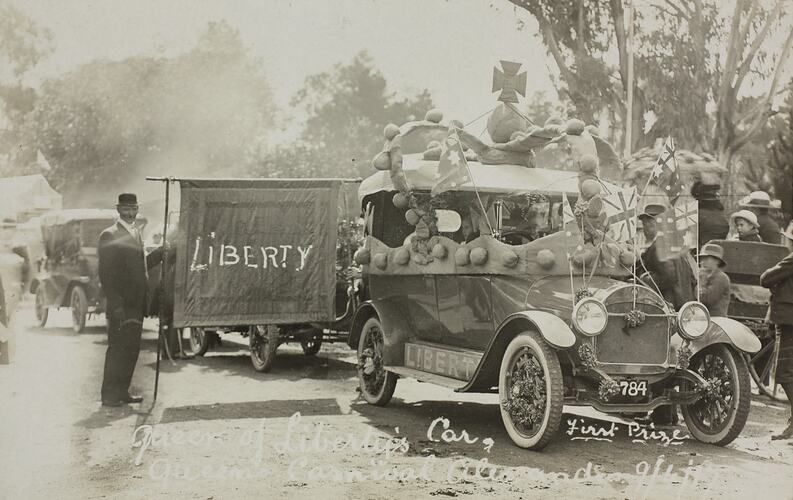Car in street parade decorated with Australian flags and a crown. Man holds flag that reads 'Liberty'.