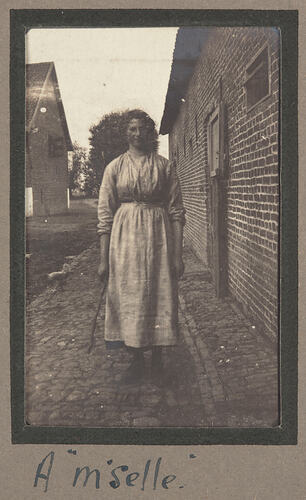 Woman in a dress standing in the street next to a brick building.