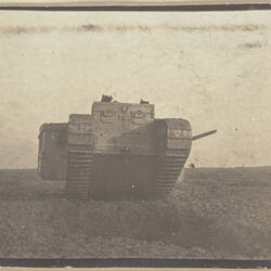 Tank in the middle of a field, with two soldiers standing to the left of the tank.