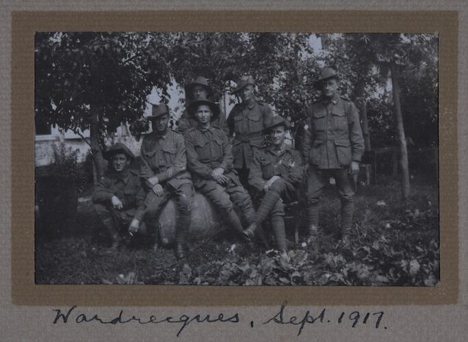 Group of servicemen in a garden with trees and house in background.