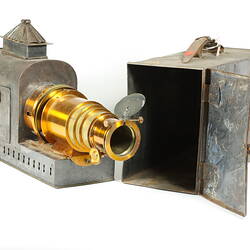 Metal box housing metal projector. Front of projector has brass telescopic cylinder.