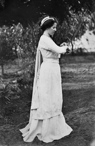 Profile of woman posing in full length white dress.