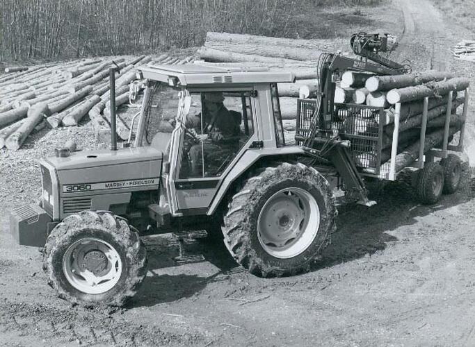 Man driving a tractor towing a forestry trailer loaded with cut logs.