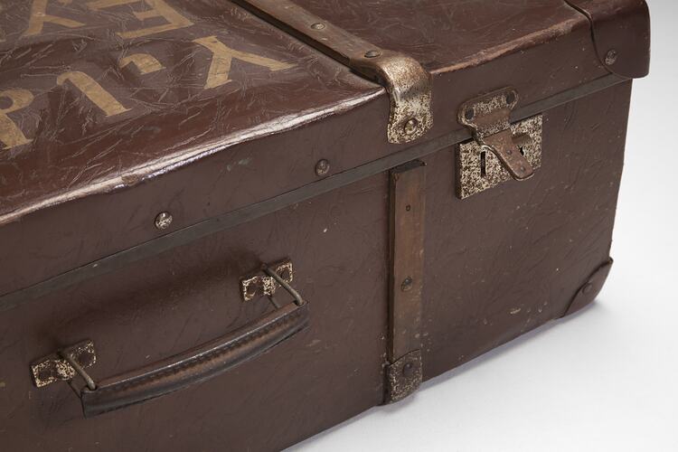 Brown hard leather suitcase detail. Part of gold text on lid, leather handle, metal lock.