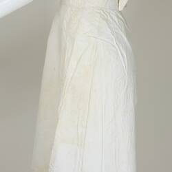 Long white cotton apron on white mannequin, side view.