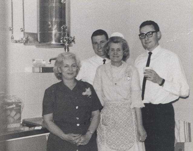 Four people in kitchen in front of urn.