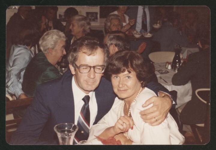 Man in glasses hugging woman in white dress.
