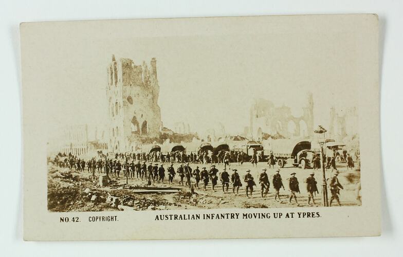 Soldiers and trucks marching along a road with ruins in the background.