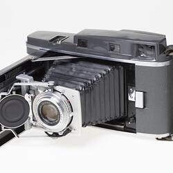 Grey steel camera with silver trim, collapsible bellows and leather handle.