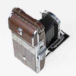 Metal folding camera with black bellows, brown leatherette wrapping and metal trim.