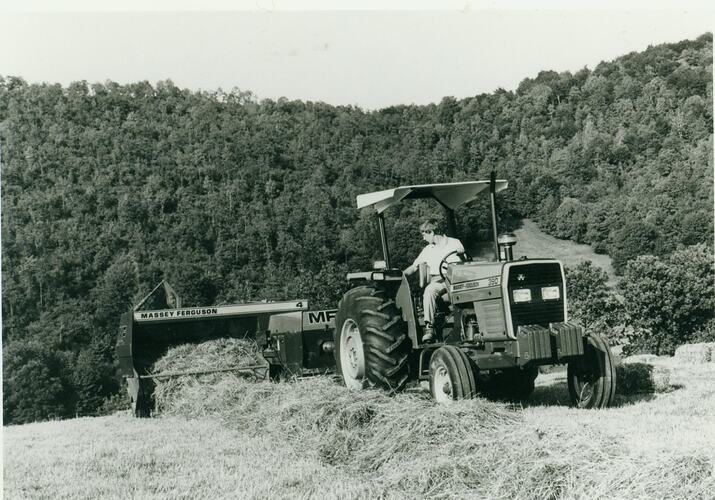 Man driving a tractor pulling a baler in a windrowed hay field.