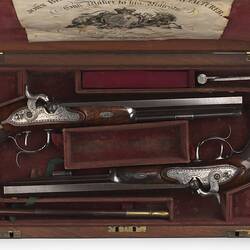 Two guns in wooden case, burgundy lining. Has seven sections. Label in lid.