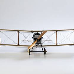 Model biplane aeroplane painted mustard brown with grey engine. Front view.