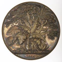 Round medal with botanical scene.