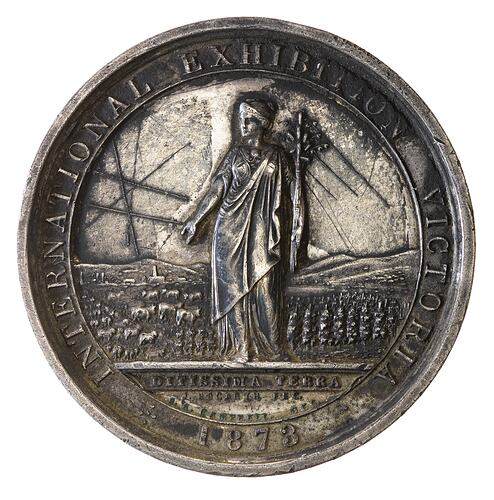Round medal with female before rural and industrial scene. Text around.