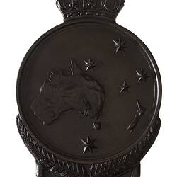 Roundish brown medal with crown atop. Features relief Southern Cross around map of Australia and New Zealand.