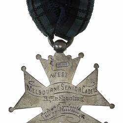 Cross shaped medal suspended from black ribbon. Engraved text.