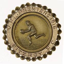Back of round gold medal, detailed edge. In centre, football player runs left holding a football.