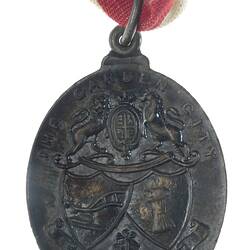 Oval medal with lion and unicorn above crossed shields. Text above and below. Red, blue, white ribbon.