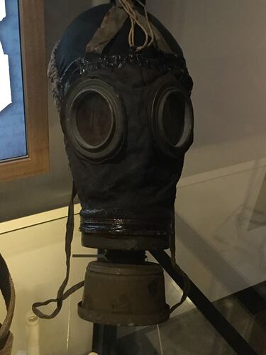 Face covering leather respirator with round, yellow lenses. Metal canister below lenses covers nose and mouth.