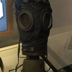 Face covering leather respirator with round, yellow lenses. Metal canister below lenses covers nose and mouth.