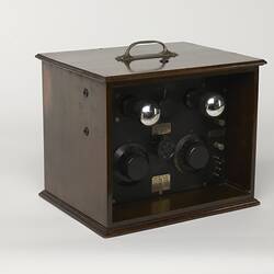 Brown wooden box with top handle. Knobs and dials on side.