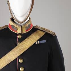 Detail of navy officer's jacket with gold sash, epaulettes. Brass buttons. Red and gold collar, white helmet.