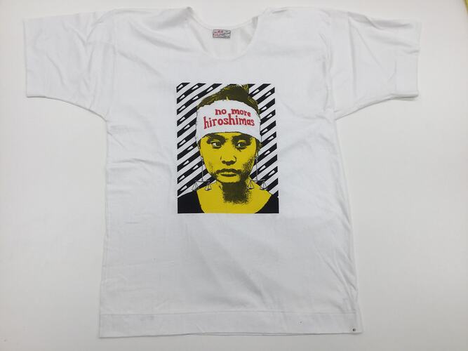 White t-shirt. Printed yellow and black face with white and red headband. Black/white diagonal lines.