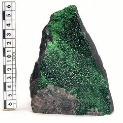 Grey rock with green crystals covering one face.