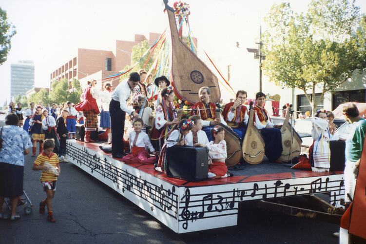 Group on a street procession float, with large instruments. They perform, wave and are wearing Ukrainian national dress.